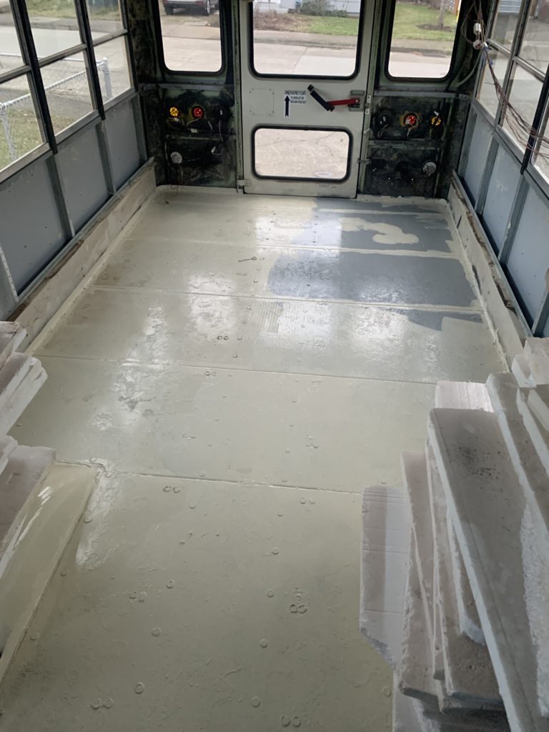 Interior of the Housebus, facing the rear door. The bus is empty, and the floor is freshly painted with high-gloss Almond-colored paint.
